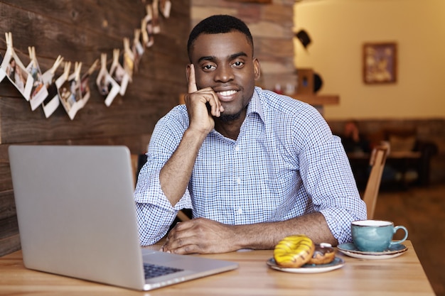 Alegre hombre de piel oscura en camisa formal que descansan en el café durante el almuerzo