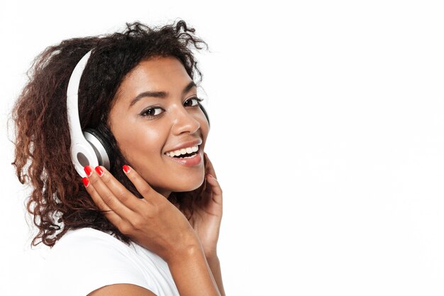 Alegre joven africana escuchando música en auriculares.