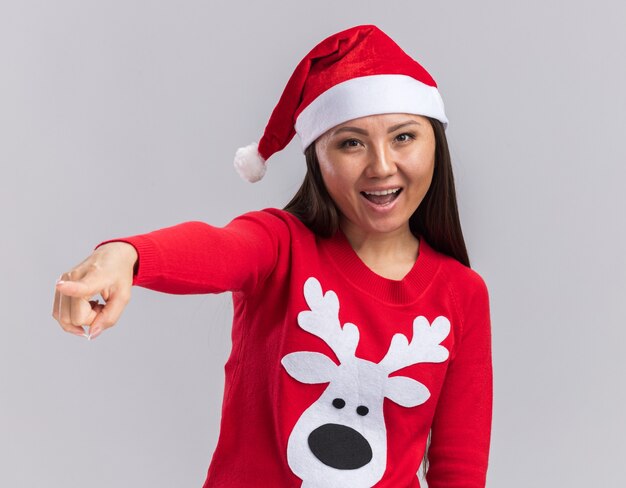 Alegre joven asiática vistiendo gorro de navidad con puntos de suéter en el lado aislado sobre fondo blanco.