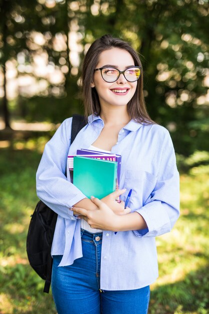 Alegre joven atractiva con libros de pie y sonriendo en el parque