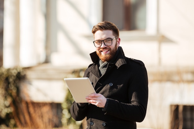 Alegre joven barbudo con tablet PC al aire libre