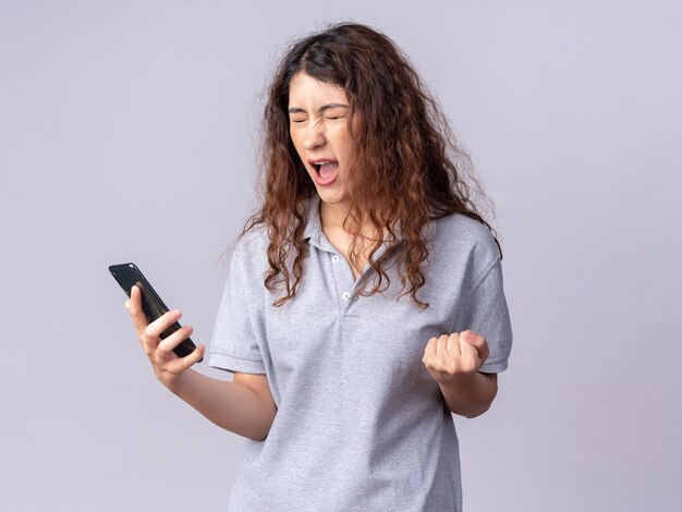 Alegre joven bastante caucásica sosteniendo teléfono móvil haciendo gesto de sí con los ojos cerrados