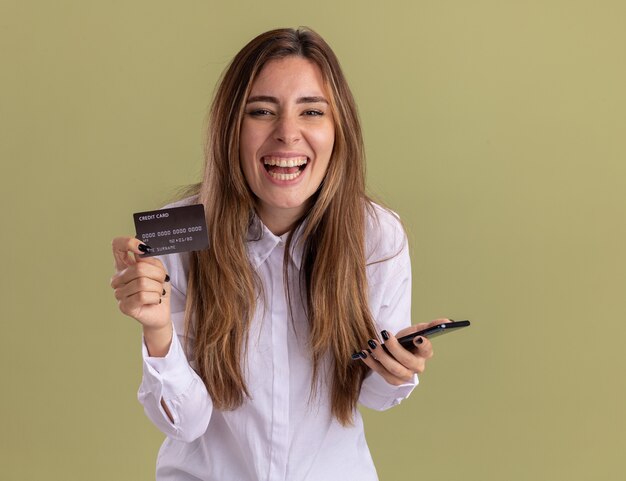 Alegre joven bastante caucásica tiene teléfono y tarjeta de crédito