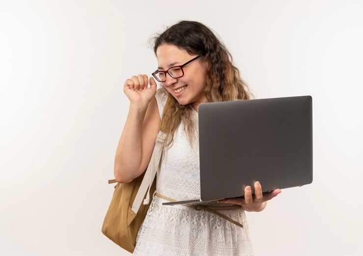 Foto gratuito alegre joven bonita colegiala con gafas y bolsa trasera sosteniendo el portátil y apretando el puño con los ojos cerrados aislado en