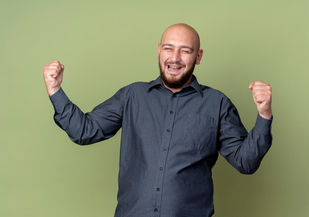 Foto gratuita alegre joven calvo call center hombre apretando los puños con los ojos cerrados aislados en verde oliva