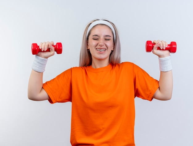 Alegre joven caucásica deportiva con tirantes con diadema y muñequeras sosteniendo pesas