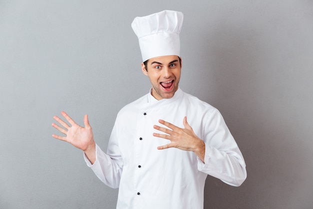 Foto gratuita alegre joven cocinero en uniforme mostrando copyspace.