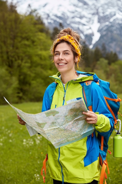 Alegre joven complacida vestida casully, lee el mapa, encuentra la ubicación necesaria, considera la ruta