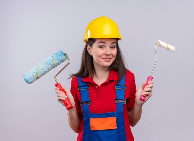 Alegre joven constructor tiene rodillos de pintura sobre fondo blanco aislado