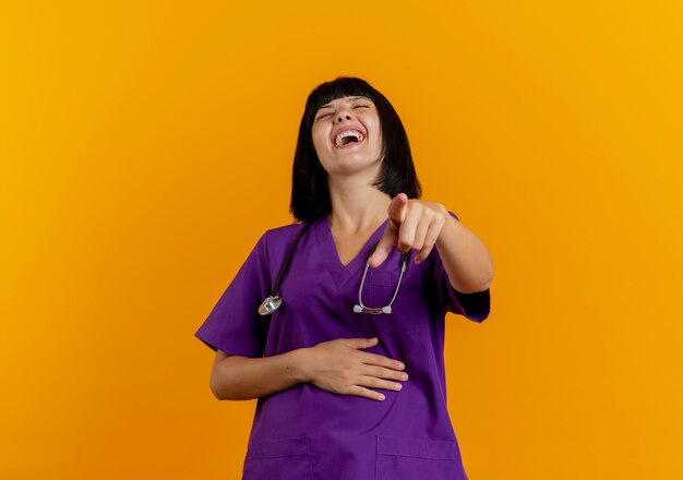 Alegre joven doctora morena en uniforme con estetoscopio riendo