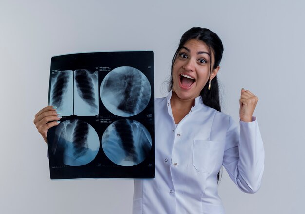 Alegre joven doctora vistiendo bata médica sosteniendo la toma de rayos x mirando haciendo sí gesto aislado