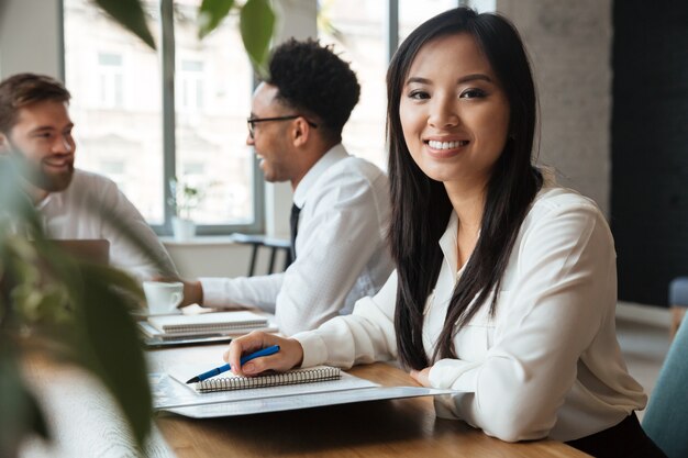 Alegre joven empresaria asiática cerca de colegas.