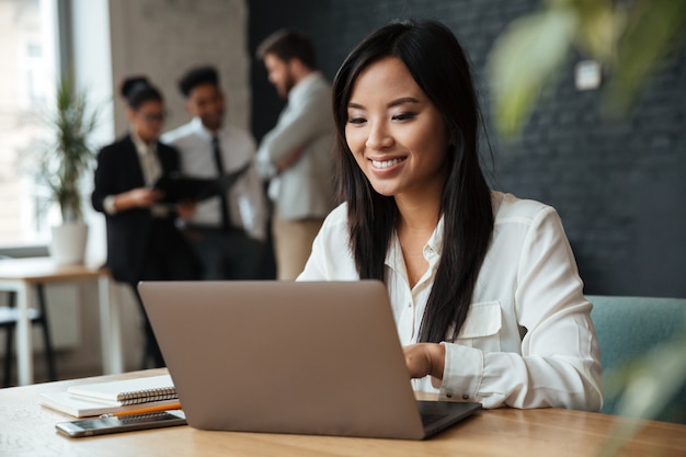 Alegre joven empresaria asiática usando laptop