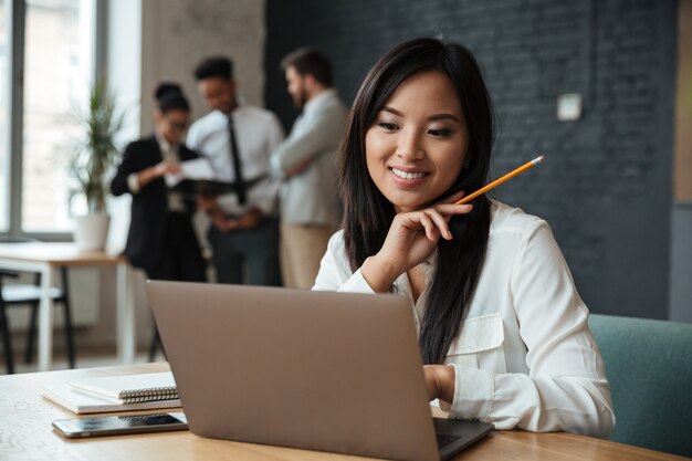 Alegre joven empresaria asiática usando laptop