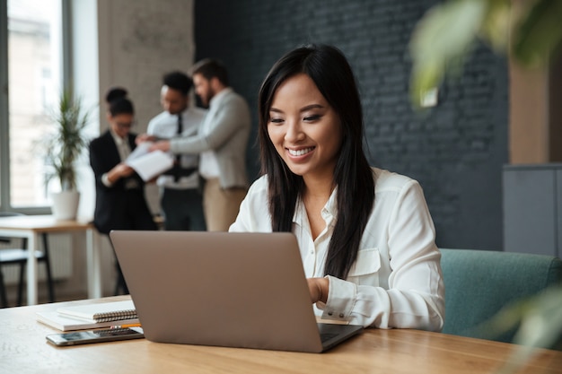 Alegre joven empresaria asiática usando laptop