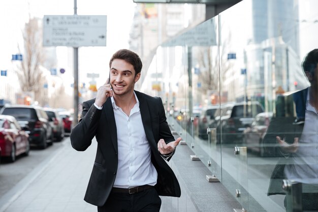 Alegre joven empresario hablando por teléfono cerca del centro de negocios