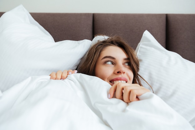 Alegre joven se encuentra en la cama en su casa debajo de una manta.