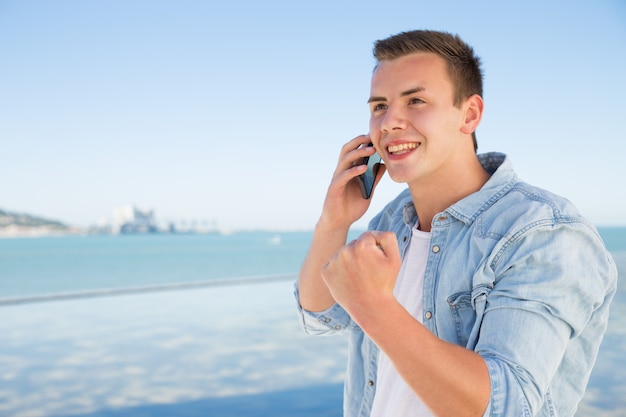 Alegre joven hablando por teléfono y mostrando gesto ganador