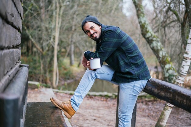 Alegre joven hipster pasando tiempo libre bebiendo café al aire libre, otoño en el país