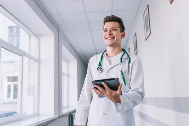 Alegre joven médico con tableta en el hall