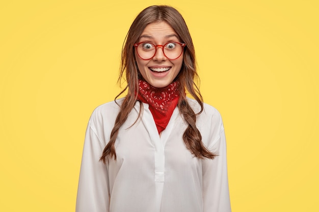 Alegre joven morena con gafas posando contra la pared amarilla