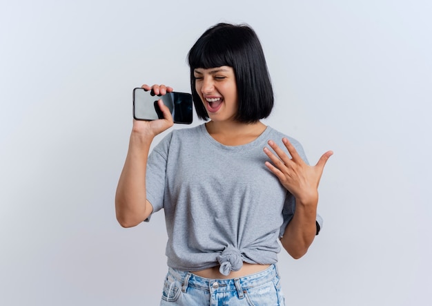 Alegre joven morena mujer caucásica sostiene teléfono fingiendo cantar