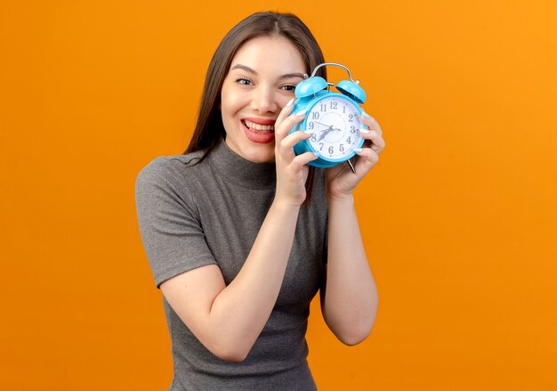 Alegre joven mujer bonita sosteniendo despertador aislado sobre fondo naranja con espacio de copia