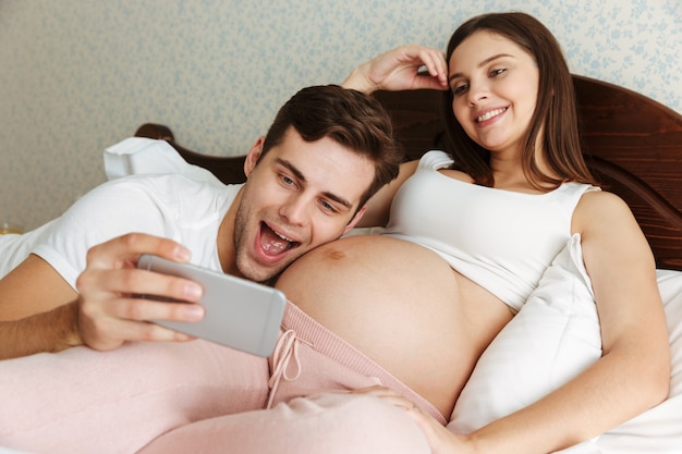 Alegre joven pareja embarazada tomando selfie