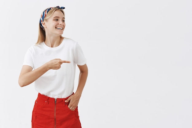 Alegre joven rubia sonriente posando contra la pared blanca