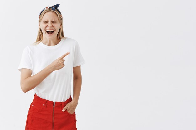 Alegre joven rubia sonriente posando contra la pared blanca