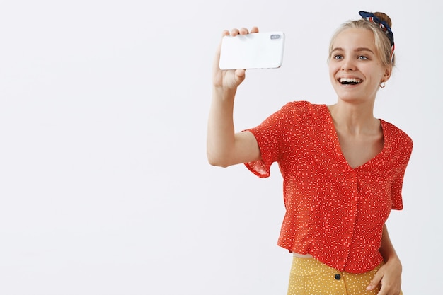 Alegre joven rubia sonriente posando contra la pared blanca