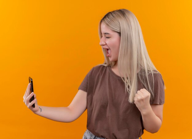 Alegre joven rubia tomando selfie con el puño levantado y los ojos cerrados en el espacio naranja aislado