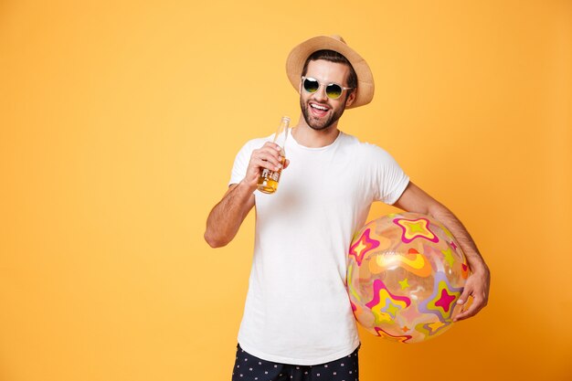 Alegre joven sosteniendo cerveza y pelota de playa