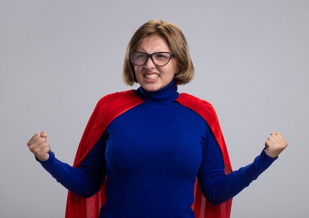 Alegre joven superhéroe rubia en capa roja con gafas mirando al lado haciendo sí gesto aislado sobre fondo blanco.