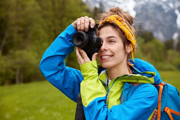 Alegre joven viajera dispara fotos con cámara profesional, disfruta caminando por el campo verde