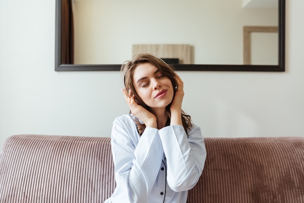 Alegre jovencita sentada en casa escuchando música