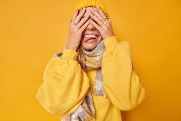 Alegre y juguetona adolescente espera sorpresa contra ojos con manos sonríe y saca la lengua viste ropa casual tontos alrededor aislado en amarillo. Concepto de emociones felices