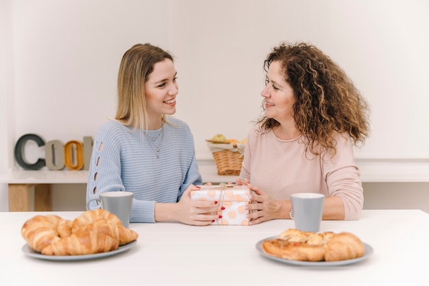 Foto gratuita alegre madre e hija con presente durante el desayuno