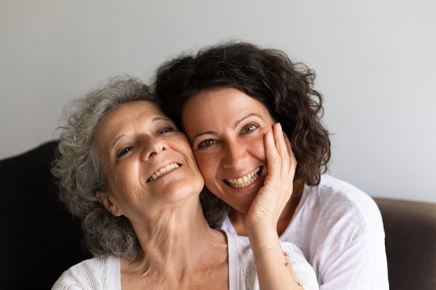 Alegre madre mayor y su hija adulta posando en casa