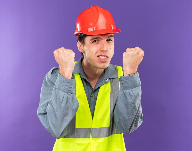 Alegre, mirando a la cámara, joven constructor hombre en uniforme mostrando sí gesto