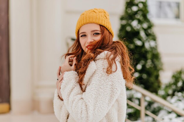 Alegre modelo femenina con cabello de jengibre posando en la calle Chica tímida de jengibre pasando el día de invierno al aire libre