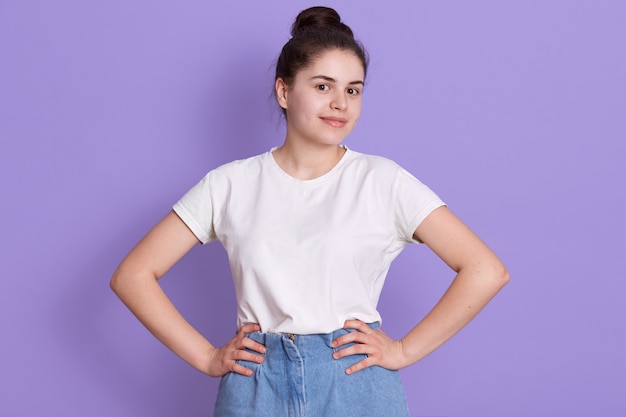 Alegre morena adolescente con moño posando contra la pared de color lila