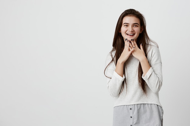 Alegre morena encantadora en suéter suelto con cabello largo y liso sonriendo alegremente