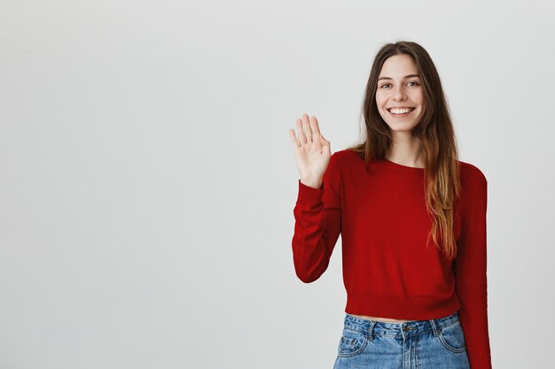 Alegre mujer atractiva amigable agitando la mano, saludando