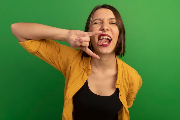 Alegre mujer bonita caucásica saca la lengua y gestos cuernos signo de mano en verde