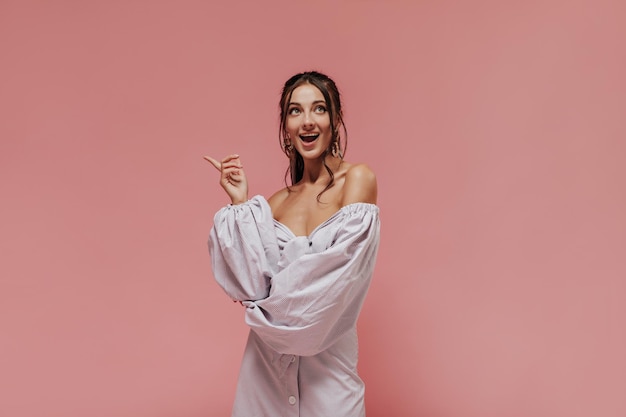 Alegre mujer de cabello negro con accesorios elegantes y ropa ligera moderna a rayas mirando hacia arriba y posando en un fondo aislado