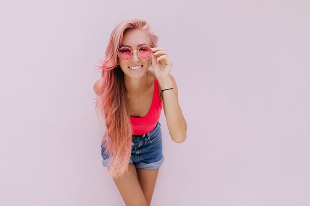 Alegre mujer caucásica con cabello rosado posando con linda sonrisa.