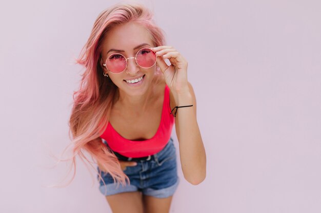 Alegre mujer caucásica con cabello rosado posando con linda sonrisa.