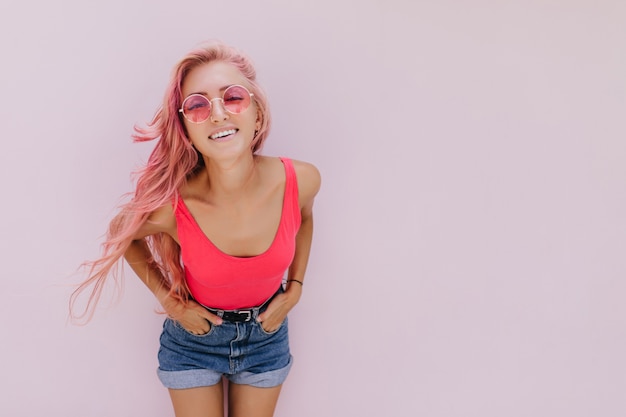 Alegre mujer caucásica con cabello rosado posando con linda sonrisa.