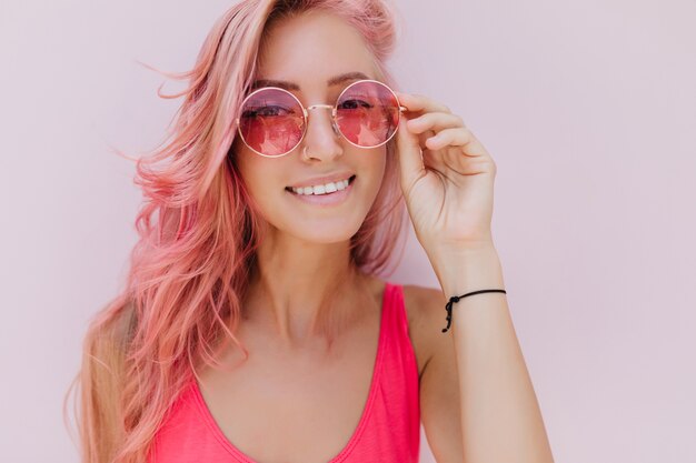 Alegre mujer caucásica con cabello rosado posando con linda sonrisa.